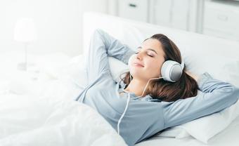 Young beautiful woman relaxing in her bed, she is listening to music and lying down with eyes closed