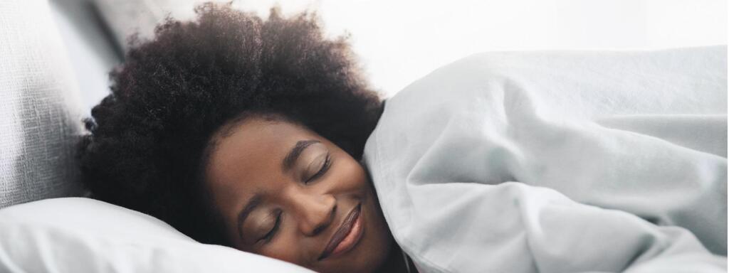 A woman in bed sleeping with a smile on her face.