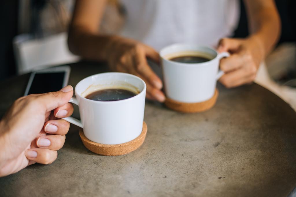 Zwei Personen sitzen gemeinsam am Tisch und halten je eine Kaffeetasse aus weißem Porzellan in der Hand.