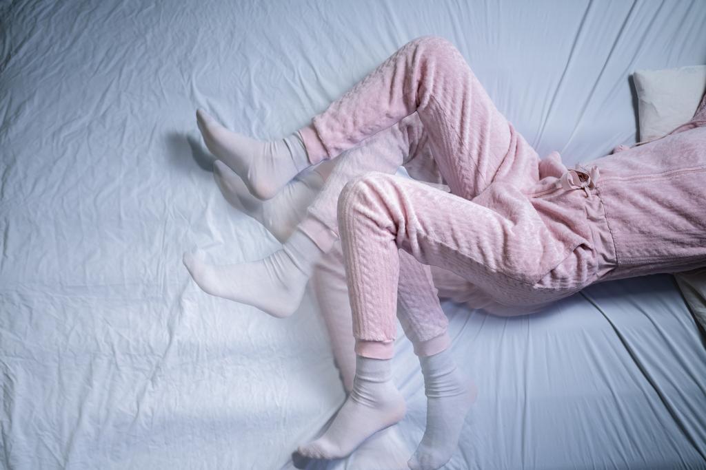 Person mit Restless Legs Syndrom in rosa Pyjama liegt auf weißem Laken im Bett und bewegt die Beine verzweifelt hin und her.