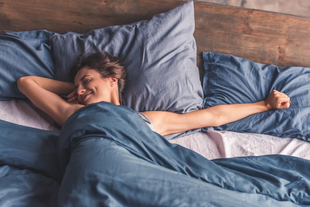 Eine junge Frau ist ausgeschlafen aufgewacht. Sie lächelt wohlig und streckt sich genüsslich im Bett.